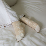 Besma from Curiously Conscious wearing white jeans and beige Paisley  ladies luxury socks from Peper Harow laying in bed.