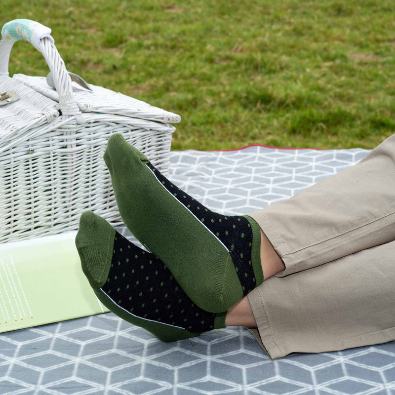 Man sitting on picnic blanket wearing tan trousers and khaki Polka organic cotton men's luxury trainer socks by Peper Harow