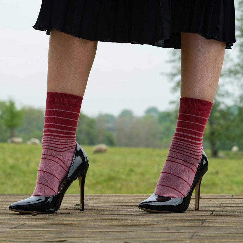 Woman standing on a deck wearing black high heels, skirt and Peper Harow musk Retro Stripe women's luxury socks