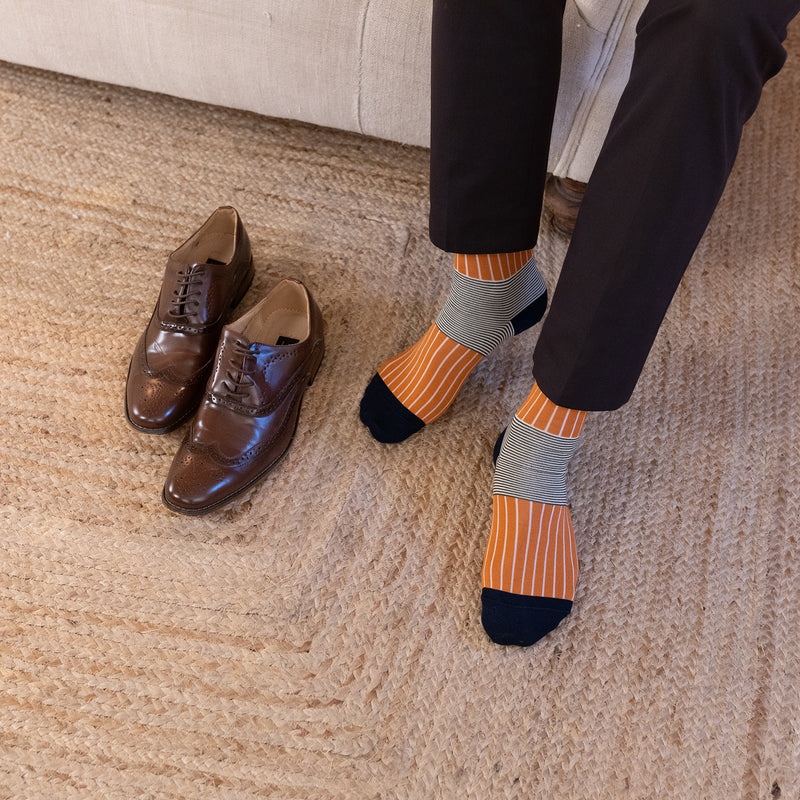 men wearing orange oxford stripe socks in black smart pants and brown shoes on the carpet