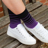 Woman sitting on a bench wearing white trainers and purple Retro Stripe ladies luxury socks from Peper Harow