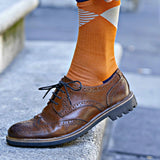 Man wearing leather oxford shoes, pulling up Orange Big Diamond socks.