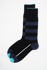 A pair of black equilibrium men's luxury socks by Peper Harow, featuring a white stripe along the foot, and three navy stripes down the calf and on the heel and toe