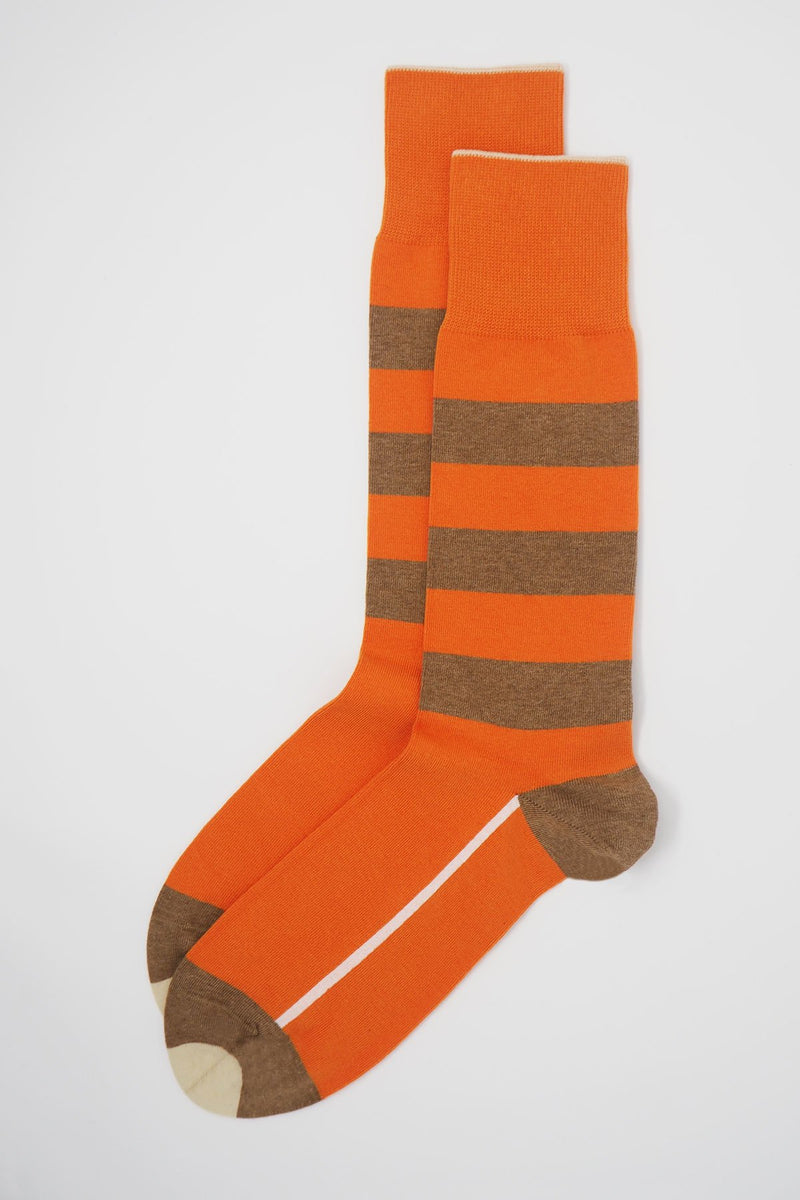 A pair of orange equilibrium men's luxury socks by Peper Harow, featuring a white stripe along the foot, and three brown stripes down the calf and on the heel and toe