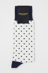 A pair of white pin polka men's socks with black polka dots and a navy heel and cuff in packaging