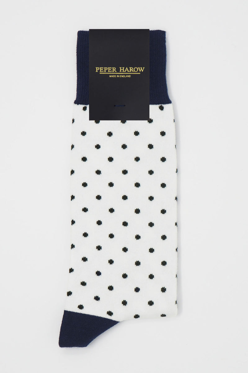 A pair of white pin polka men's socks with black polka dots and a navy heel and cuff in packaging