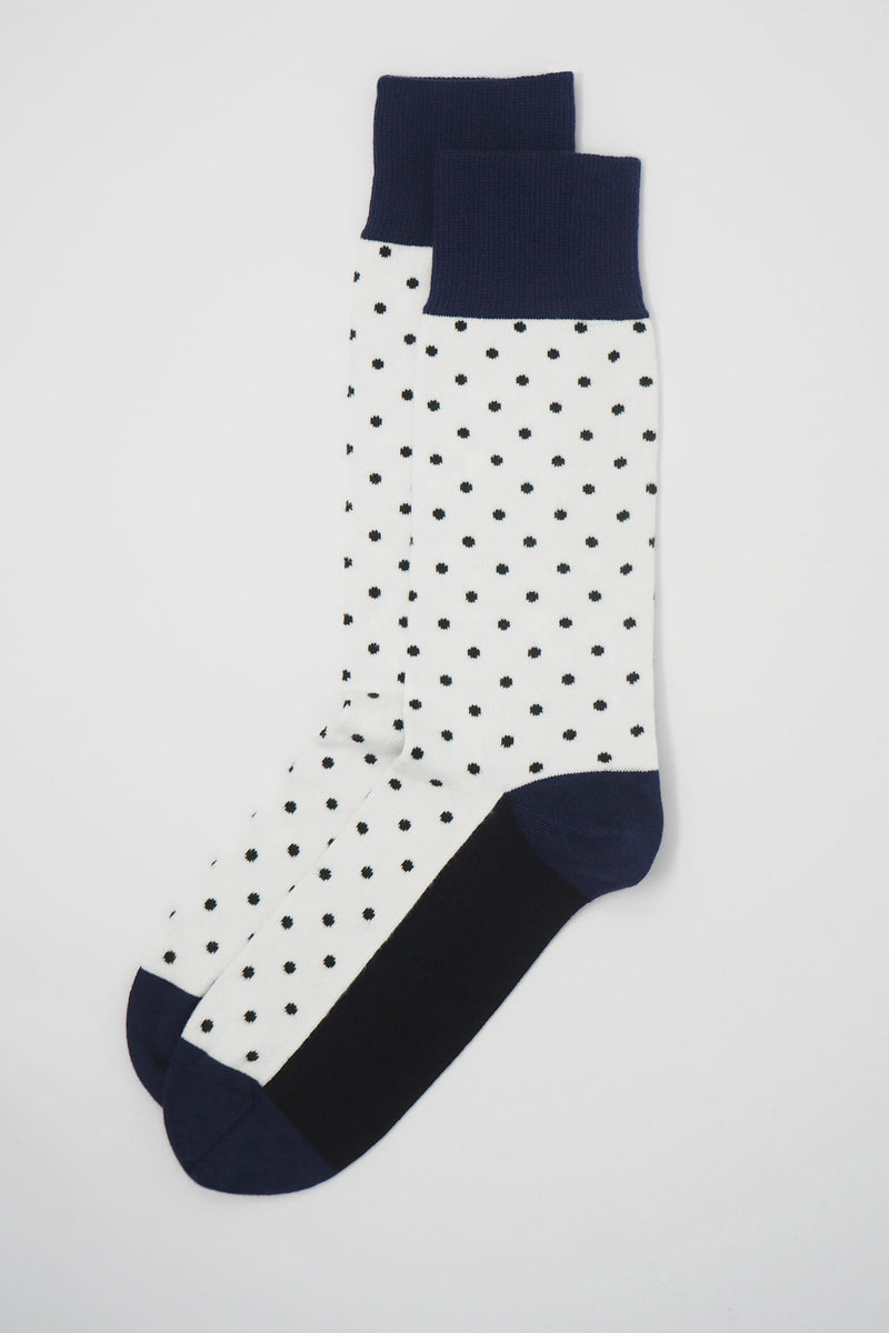 A pair of white pin polka men's socks with black polka dots and a navy heel, toe and cuff
