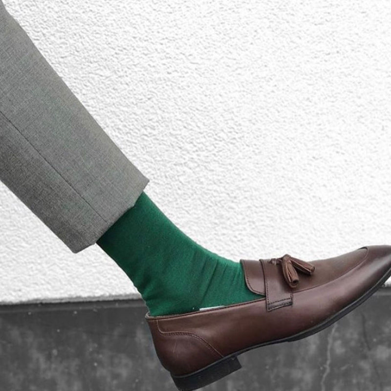 Man in grey trousers and brown loafers wearing Peper Harow emerald Square Mile luxury socks