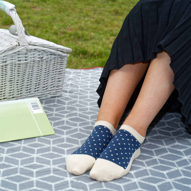 Woman in a black skirt having a picnic in a field wearing Peper Harow beige Organic Polka luxury women's trainer socks