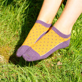Woman sitting on grass wearing berry Polka Organic luxury trainer socks