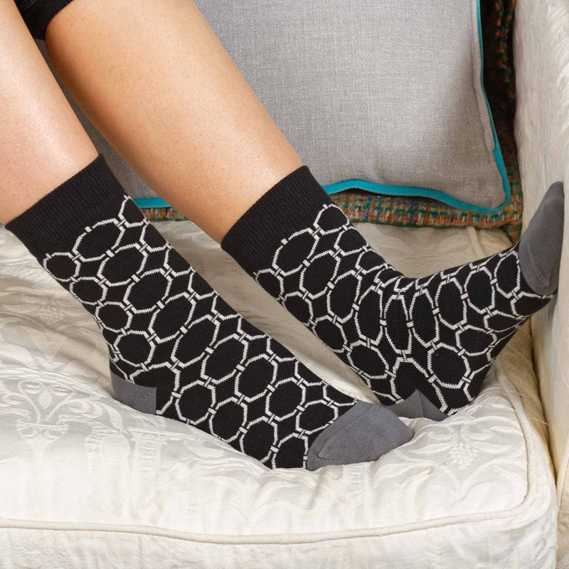 Woman sitting on a sofa wearing black Beehive women's luxury socks from Peper Harow