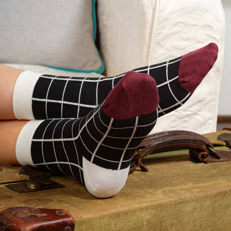Woman sitting on sofa wearing Peper Harow black Grid women's luxury socks