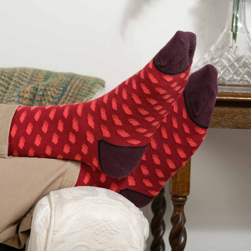 Man laying on sofa wearing tan trousers and burgundy Disruption men's luxury socks from Peper Harow