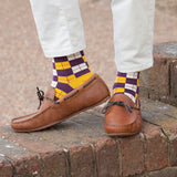 Man standing on a wall wearing brown boat shoes and Peper Harow gold checkmate luxury men's socks