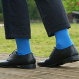 Man walking outside wearing chinos, smart black shoes and blue classic plain men's luxury socks from Peper Harow