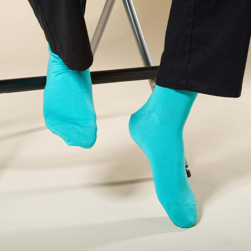 Man sitting on stool wearing black trousers and turquoise Classic men's luxury socks