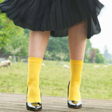 Woman wearing black high heels, a black skirt and Peper Harow yellow Classic women's luxury socks