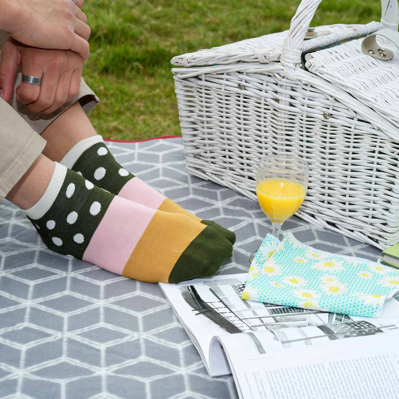 Man sitting on picnic blanket wearing tan trousers and cream Mayfair luxury trainer socks by Peper Harow