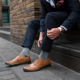 Man sitting on stairs wearing grey Lux Taylor men's luxury socks and brown shoes with a navy suit