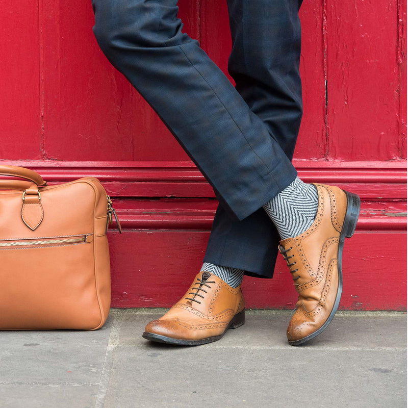 Man wearing grey Lux Taylor Peper Harow luxury socks and brown brogues standing against a red wall