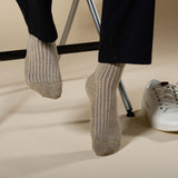 Man sitting on a stool wearing black trousers and beige Recycled Ribbed men's recycled cotton socks by Peper Harow