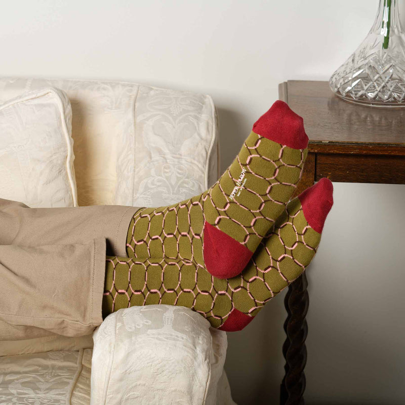 Man laying on sofa wearing tan trousers and olive Linked men's luxury socks by Peper Harow