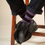 Man sitting on wooden stool wearing purple Equilibrium luxury organic cotton socks by Peper Harow and black leather shoes