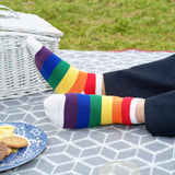 Man sitting on a picnic blanket wearing black trousers and Peper Harow rainbow Block Stripe men's luxury trainer socks