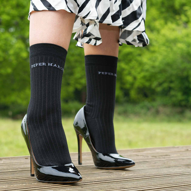 Woman wearing black high heels, zebra print skirt and Peper Harow recycled ribbed women's socks in black