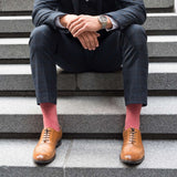Man sitting on stairs wearing a navy suit, brown shoes and red Lux Taylor men's luxury socks by Peper Harow
