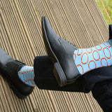 Man sitting on a deck wearing black shoes, navy trousers and Peper Harow blue Linked luxury socks