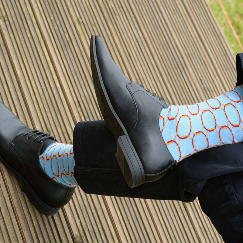 Man sitting on a deck wearing black shoes, navy trousers and Peper Harow blue Linked luxury socks