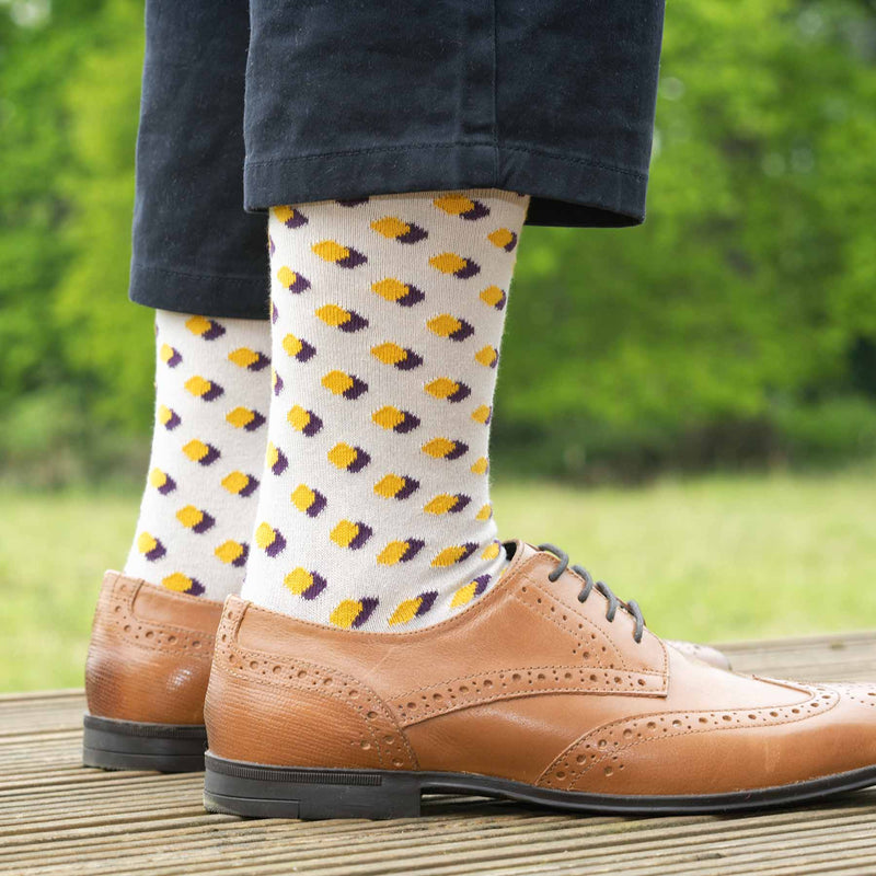 Man standing on a deck wearing brown shoes, navy trousers and Peper harow taupe Disruption men's luxury socks