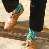 Man walking down stairs wearing brown shoes, black trousers and teal Septem men's luxury socks by Peper Harow