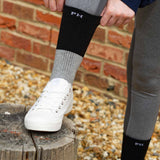 Woman wearing grey leggings, white trainers and pulling up her black Recycled women's sport socks by Peper Harow