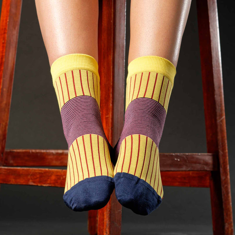 Woman sitting on wooden stool wearing yellow Oxford Stripe luxury ladies socks by Peper Harow